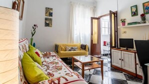 A living room with a sofa, a coffee table, a TV, and a kitchen area with cabinets. - Apartamento La Perla flamenca (Cádiz)