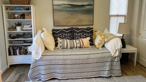 Een slaapkamer met een bed, een boekenkast, een raam en een schilderij aan de muur.