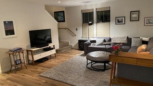 Een moderne woonkamer met een flatscreen televisie, een grijze bank, een salontafel en een trap naar een bovenverdieping.