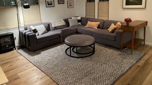 Een moderne woonkamer met een modulaire bank, een ronde salontafel en een klein houten bijzettafeltje met een bloevas.