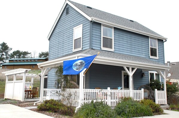 A two-story house with a blue exterior, white porch, and a blue flag with a white emblem. - Point Reyes Station Vacation Home: Close to Town (Point Reyes Station)
