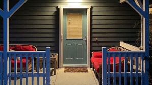A porch with a blue door, a small table, and two red chairs.