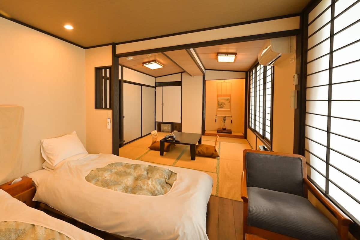 A traditional Japanese-style hotel room with tatami flooring, a futon bed, a desk with a chair, and sliding doors.