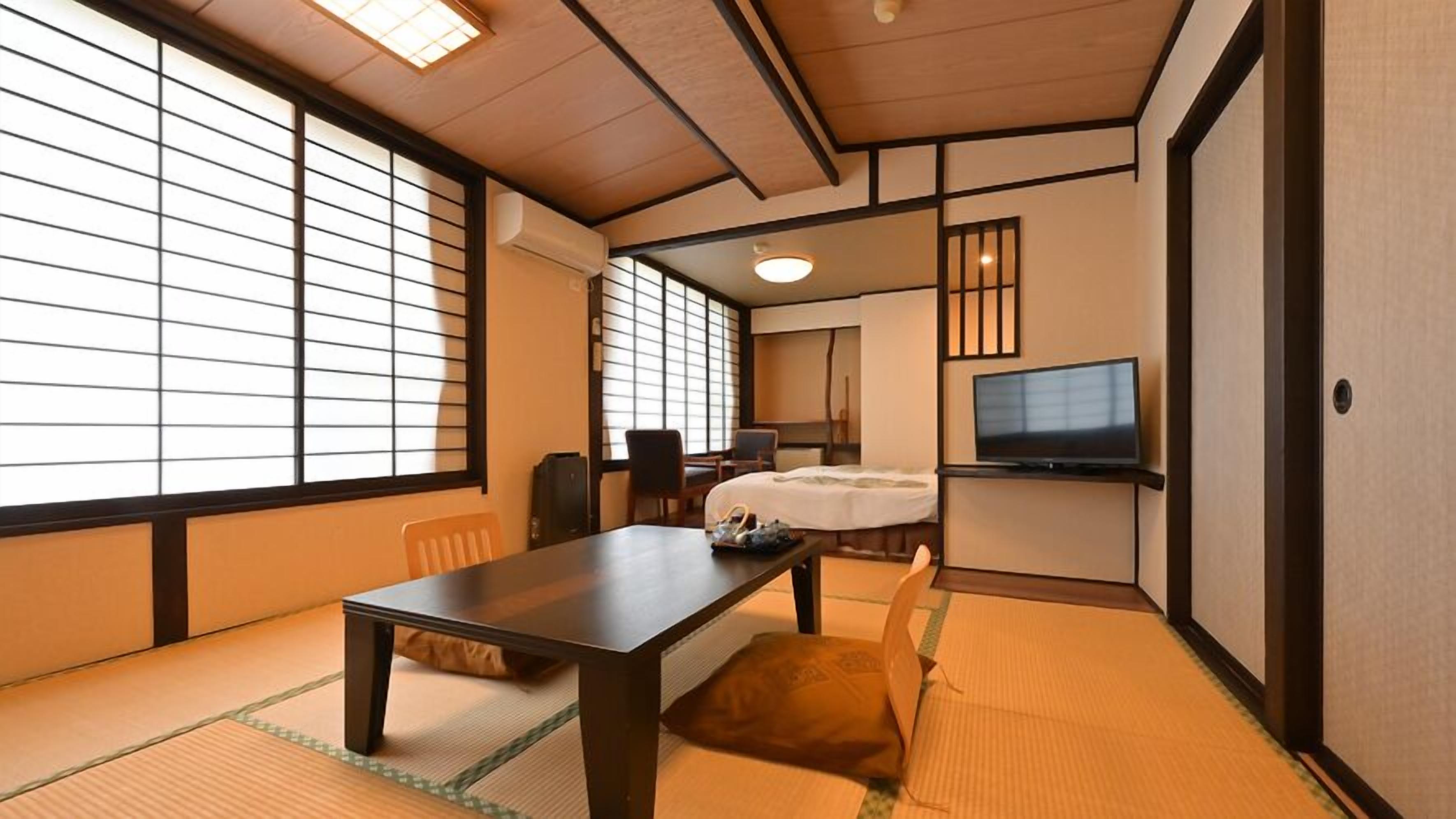A traditional Japanese-style room with tatami flooring, a low table, a bed, and a television.