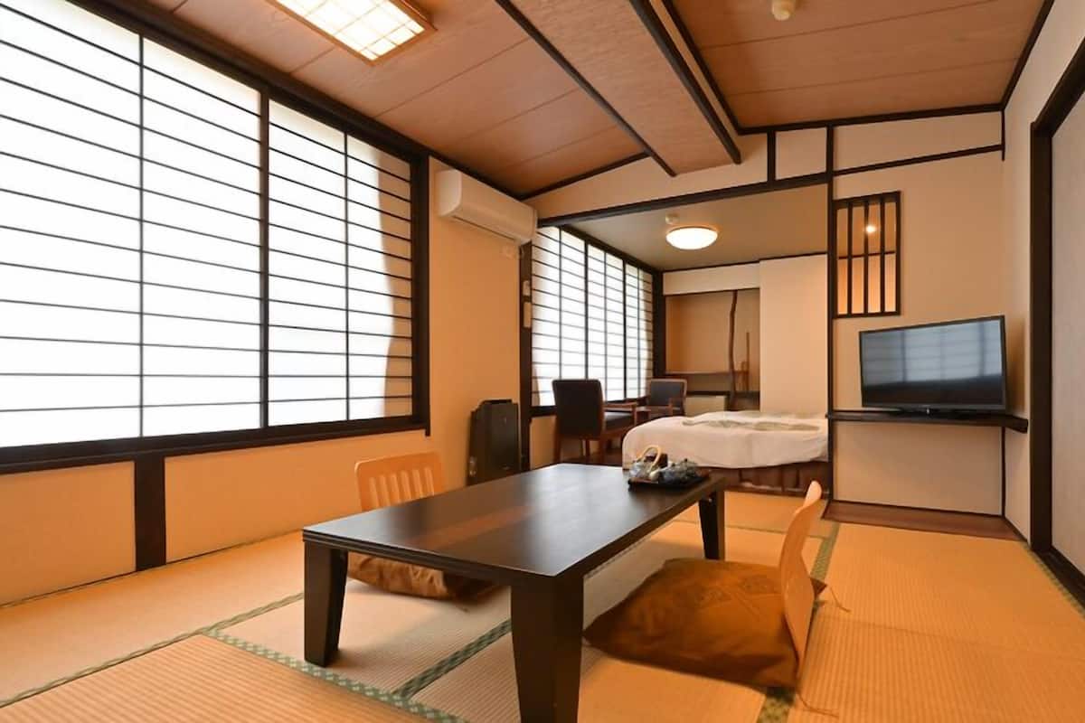 A traditional Japanese-style room with tatami flooring, a low table, a bed, and a television.