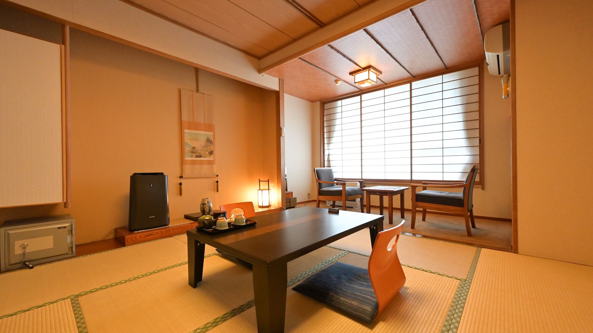 A traditional Japanese room with tatami flooring, a low table, chairs, a heater, and a window with shoji screens.