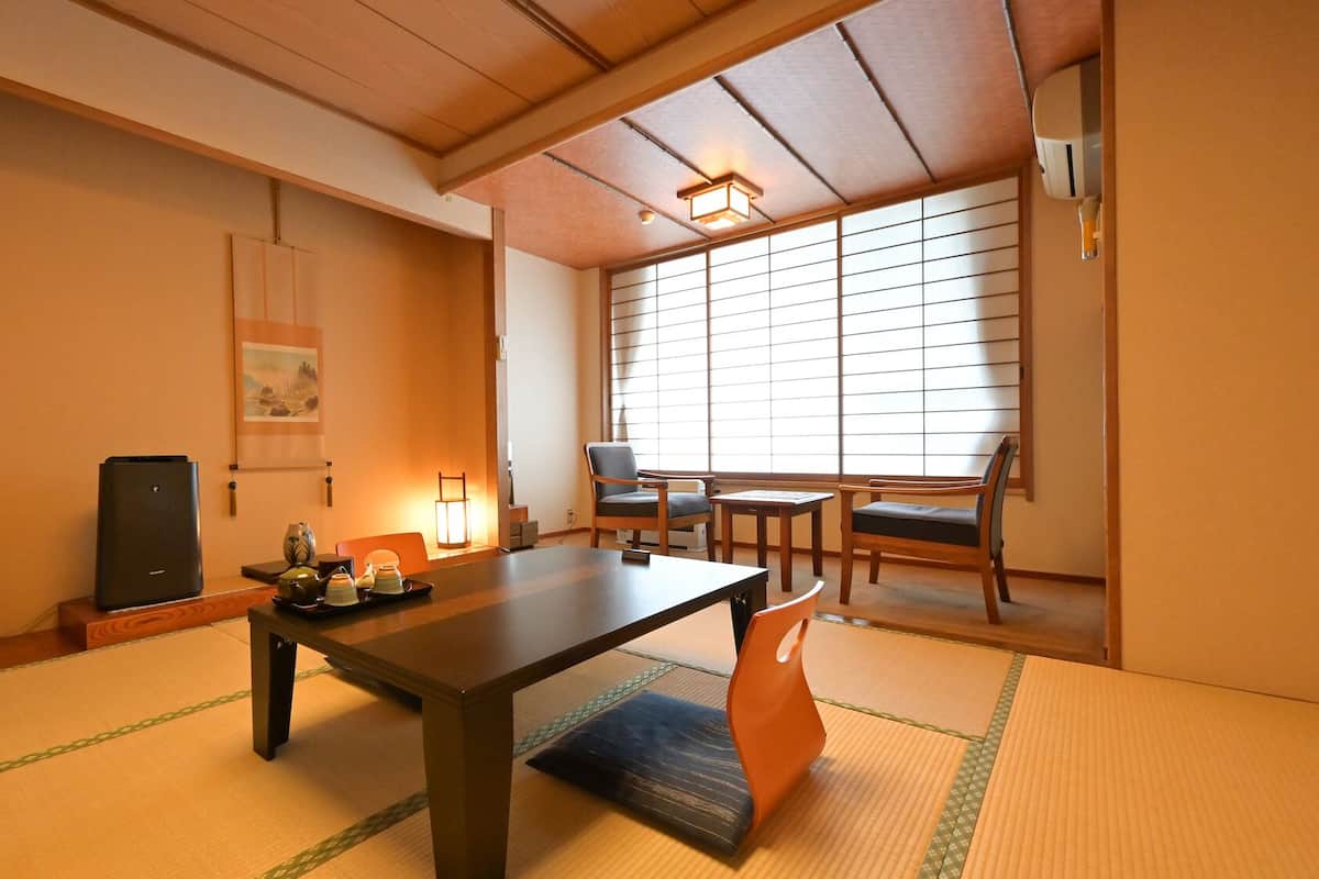 A traditional Japanese room with tatami flooring, a low table, chairs, a heater, and a window with shoji screens.