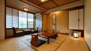 A traditional Japanese room with tatami flooring, a low table with cushions, and sliding doors. - Ryokan Tamura (Kusatsu)