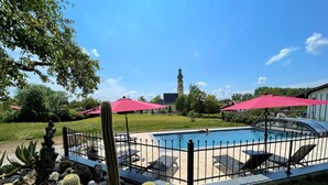 Piscina cercada por gramado, cadeiras de descanso e plantas em vasos.