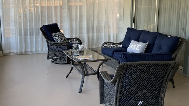 Un balcon agrémenté de meubles en osier, notamment d’un canapé et de fauteuils, ainsi que d’une table basse en verre.