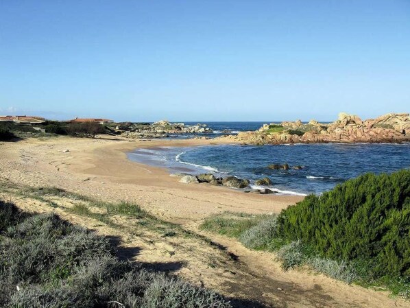 Paisagem costeira com uma praia de areia, afloramentos rochosos e vegetação densa.
