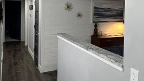 Un couloir avec un plafond orné de poutres en bois, un mur blanc sur lequel est accrochée une peinture, et un comptoir en marbre.