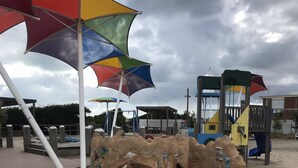 Ett sandigt strandområde med en träbänk och färgglada parasoller.
