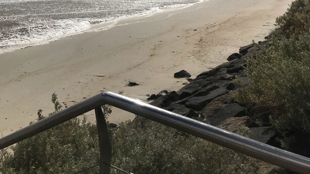 En strand med en vågbrytare av sten och ett metallräcke i förgrunden.