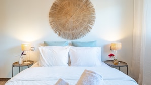 Una cama bien hecha con sábanas blancas, dos mesitas de noche con lámparas y un adorno circular grande en la pared.