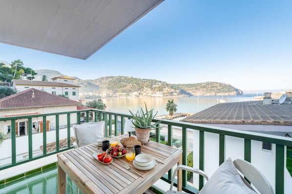 A balcony with a table set for breakfast, overlooking a coastal view with buildings and hills.