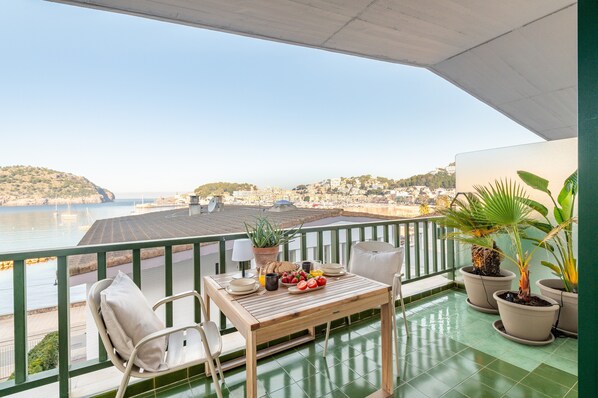 Ein Balkon mit Esstisch, Blumentöpfen und Blick auf das Meer und Gebäude.