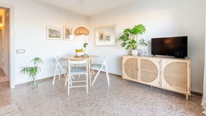 Una sala de estar moderna con una mesa de comedor, sillas, un televisor sobre un mueble de madera y cuadros enmarcados en la pared.