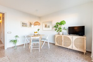 A modern living room with a dining table, chairs, a television on a wooden cabinet, and framed pictures on the wall.