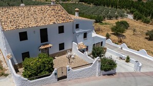 Edifici blanc amb teulada de rajola, envoltat per una paret blanca i un jardí amb un arbre petit i una banca.