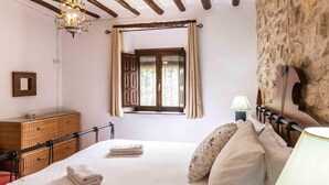 Un dormitori amb un llit, una làmpada de nit, una finestra amb cortines, un taulell de nit de fusta i un mirall a la paret.