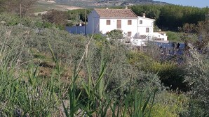 Edifici blanc amb teulada enrajolada, envoltat de vegetació i amb turons al fons.