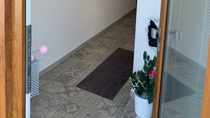 Un pasillo con baldosas de diseño, un tapete oscuro, luminarias fijadas a la pared y una puerta con panel de vidrio.