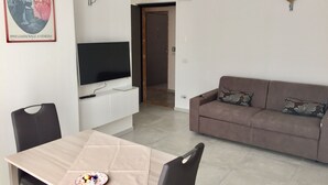 Una sala de estar con televisor, sofá y mesa de comedor.