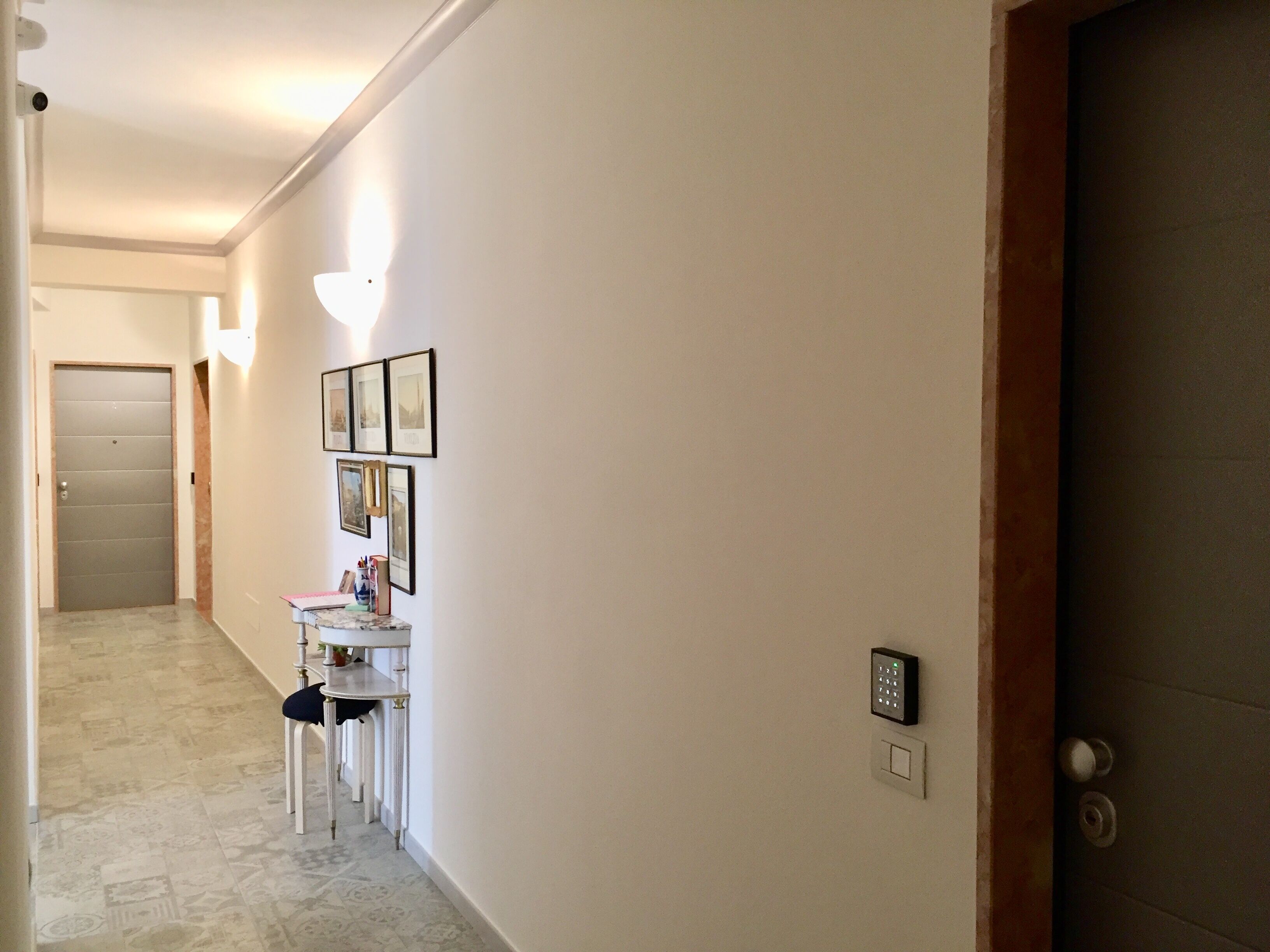 A hallway with a marble floor, a door, a small table with a vase, and framed pictures on the wall.