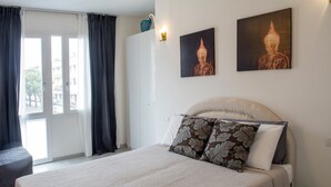 Una habitación de hotel con cama, una silla, una ventana con cortinas y dos cuadros colgados en la pared.
