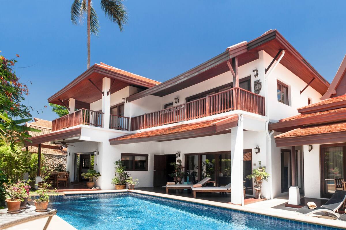 A two-story house with a swimming pool, balconies, and outdoor furniture.