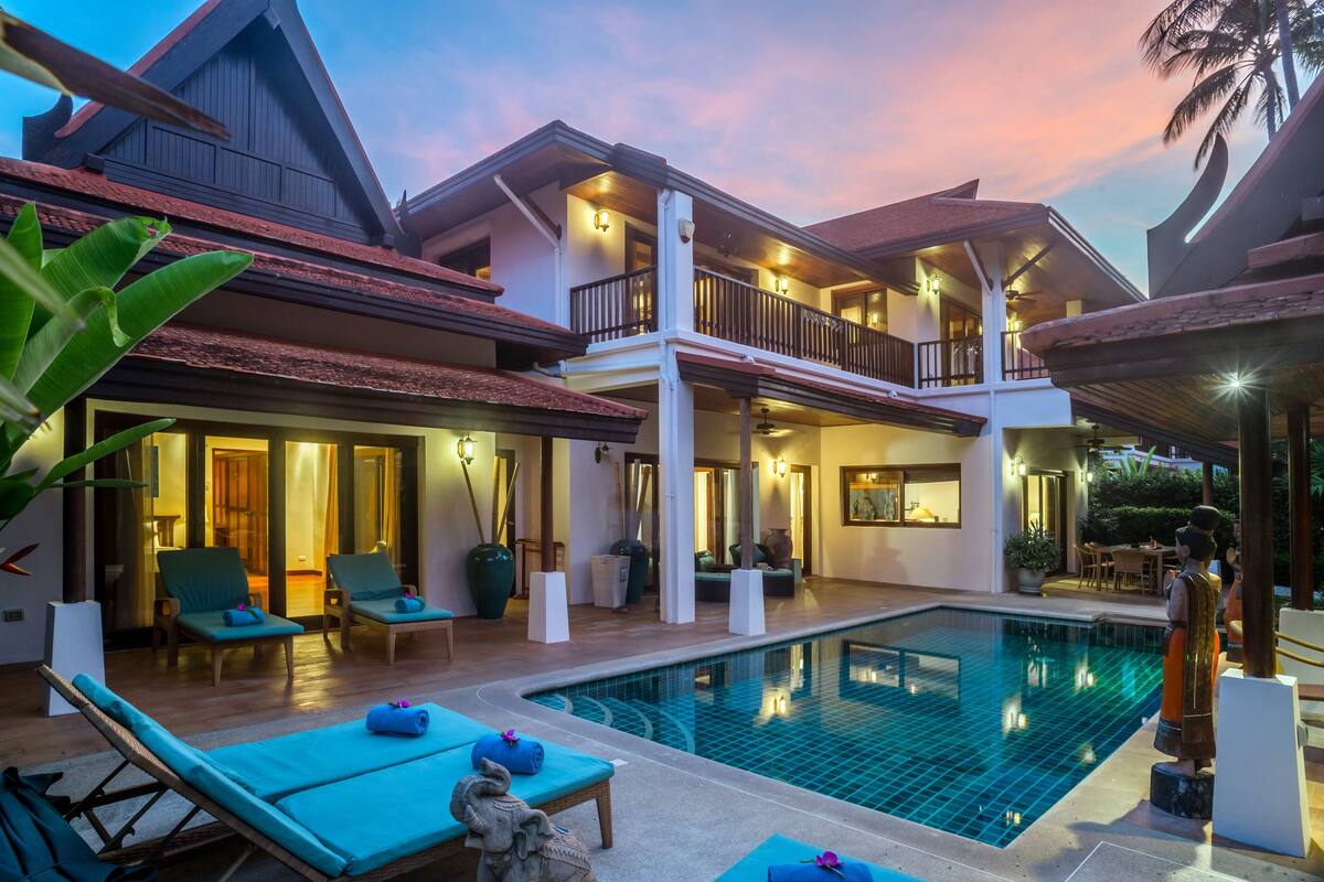 A two-story building with a swimming pool, lounge chairs, and a statue.