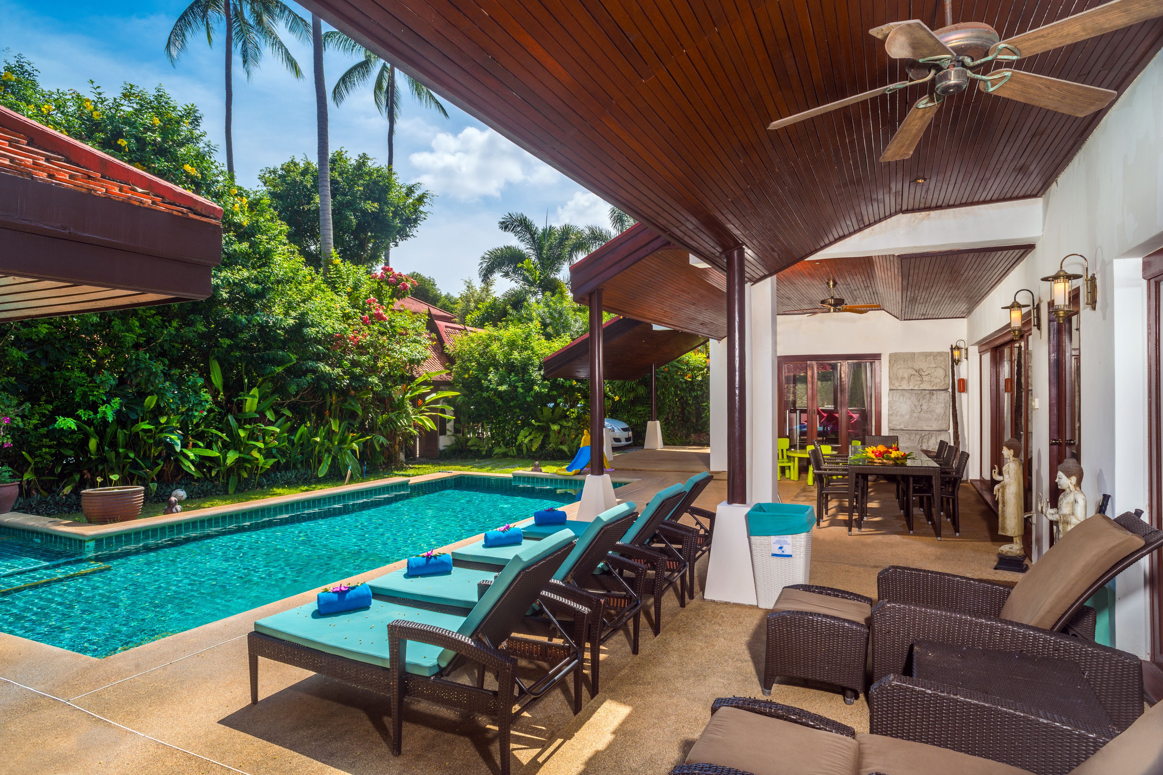A poolside area with lounge chairs, a dining table, and a ceiling fan.