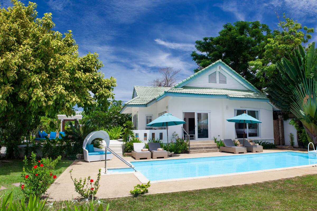 A house with a swimming pool, surrounded by lush greenery and a clear blue sky.