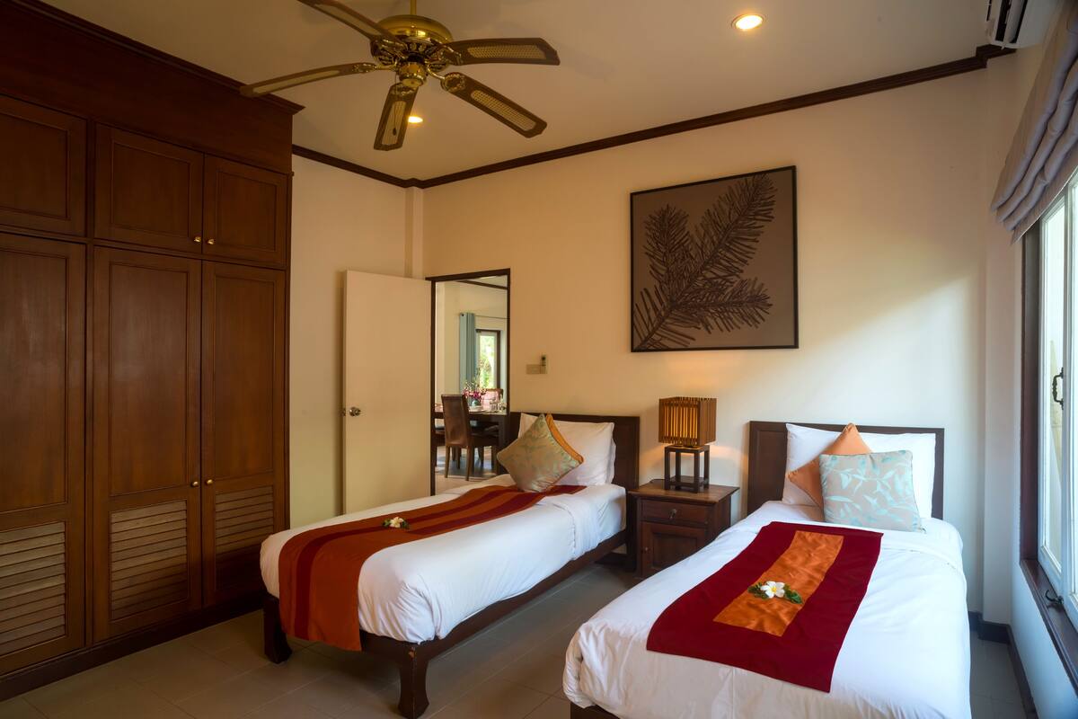 A hotel room with two beds, a ceiling fan, a large mirror, and a window with curtains.