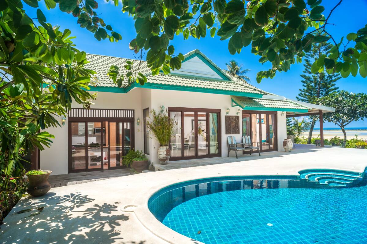 A modern house with a swimming pool, large windows, and a view of the beach.