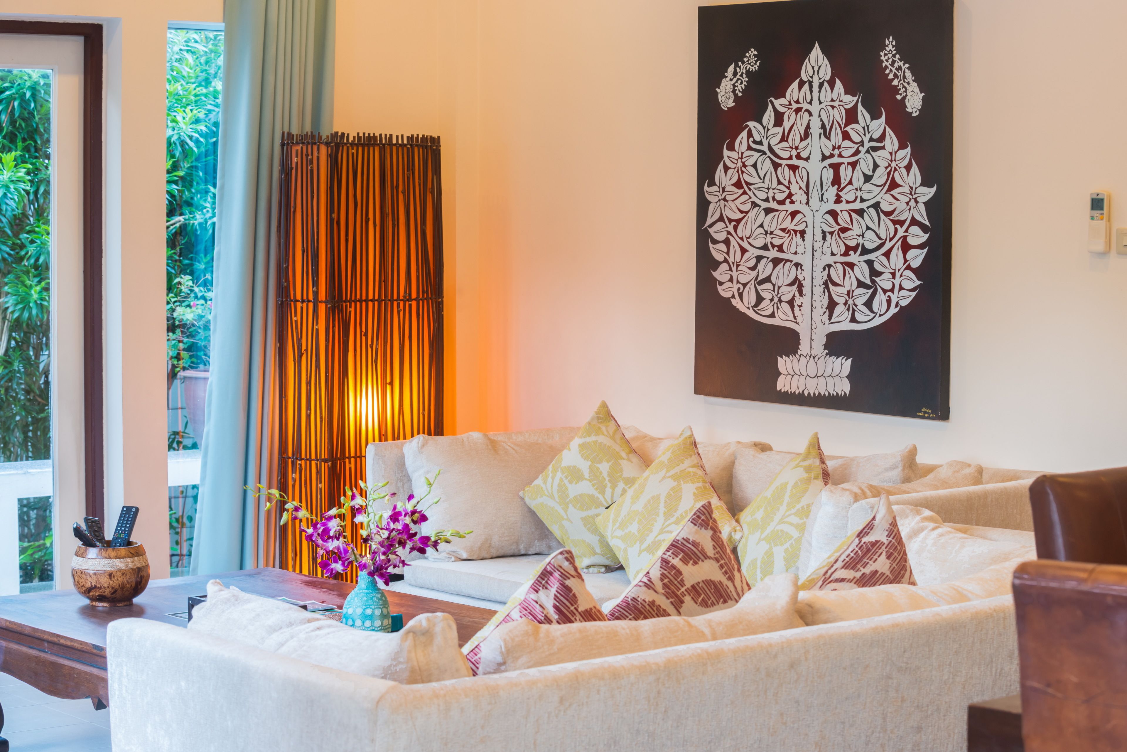 A living room with a sofa, cushions, a vase with flowers, and a wall-mounted artwork.