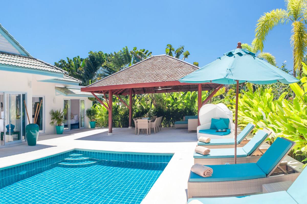 A modern house with a swimming pool, outdoor furniture, and tropical plants.
