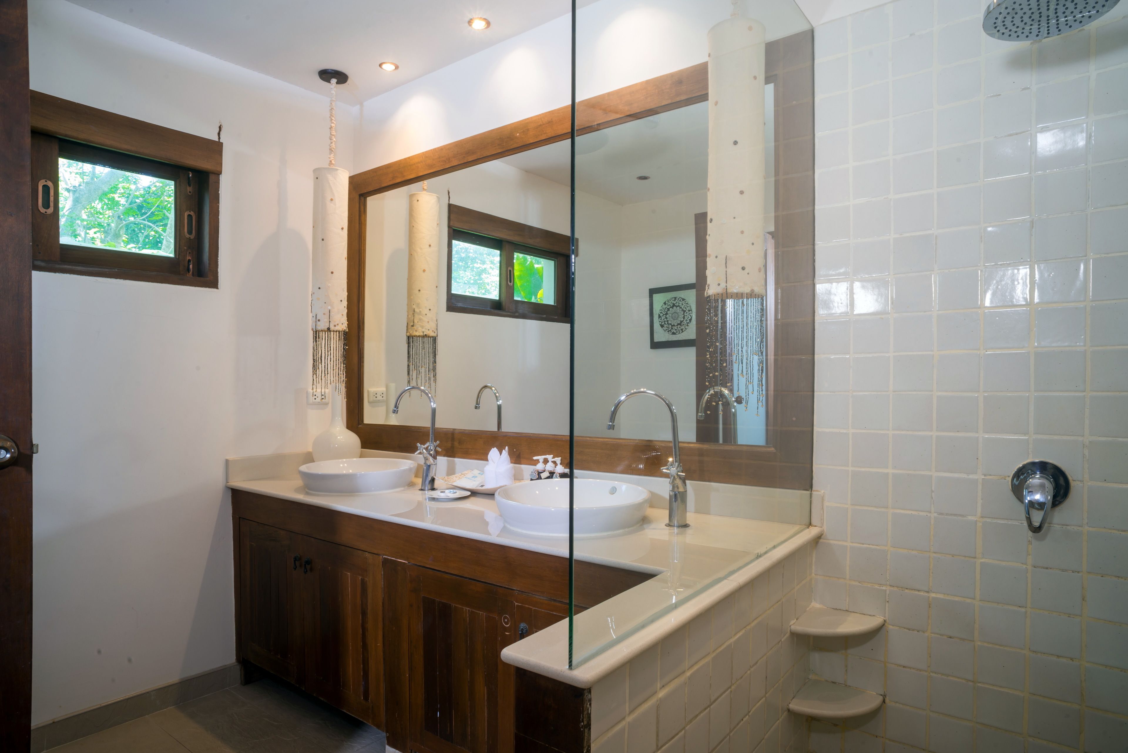 A bathroom with a wooden vanity, two sinks, a large mirror, and a shower area.