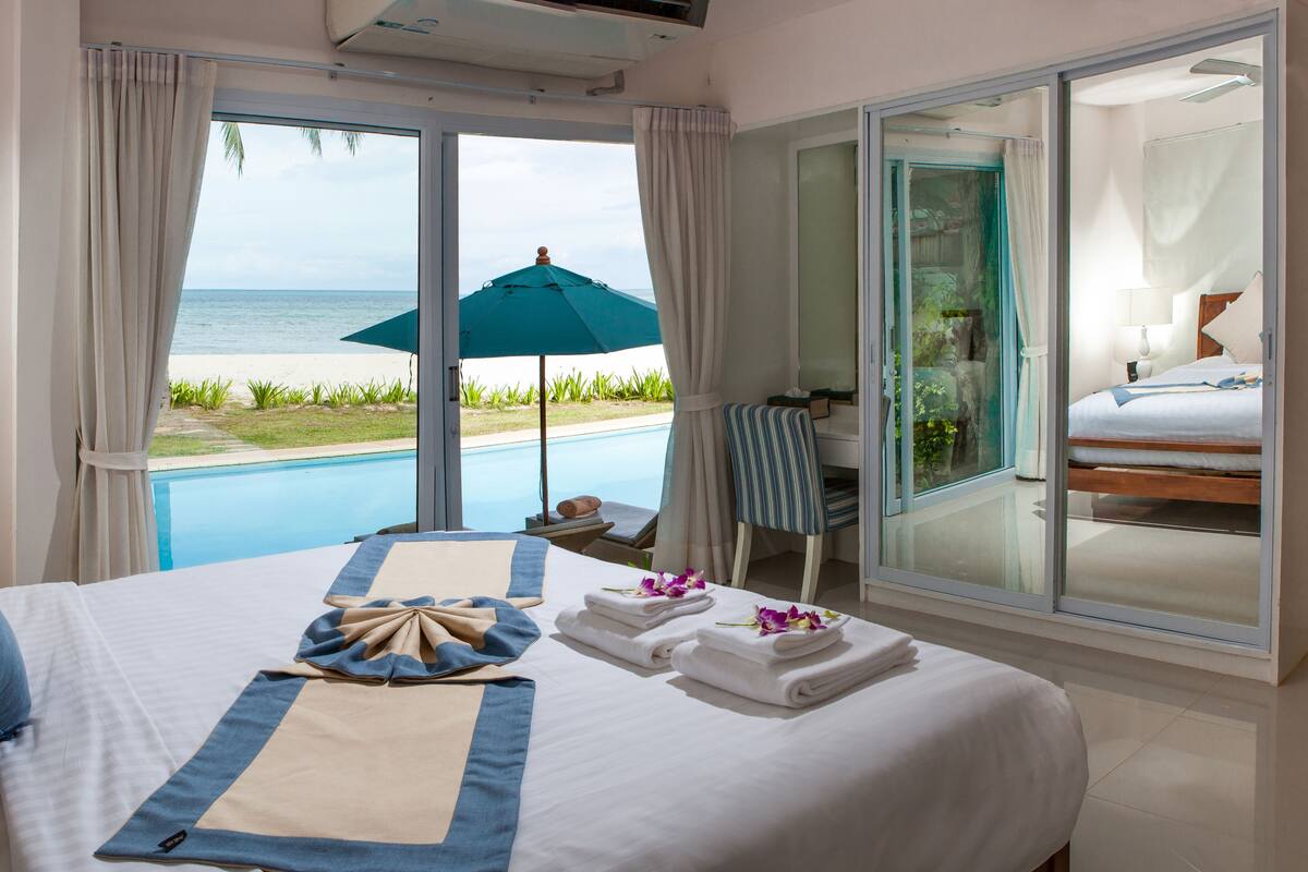 A hotel room with a large bed, a view of the ocean, a pool, and a sliding glass door leading to a balcony.