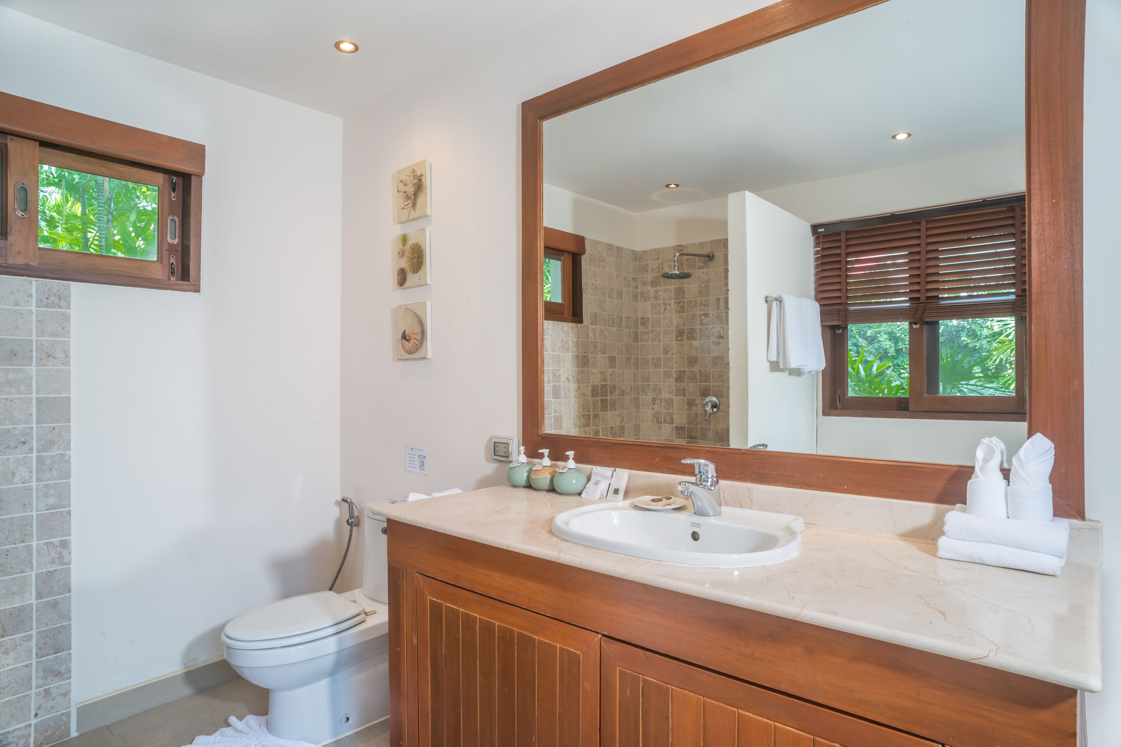 Ein Badezimmer mit Toilette, Waschbecken mit Spiegel und einem Fenster mit Jalousien.