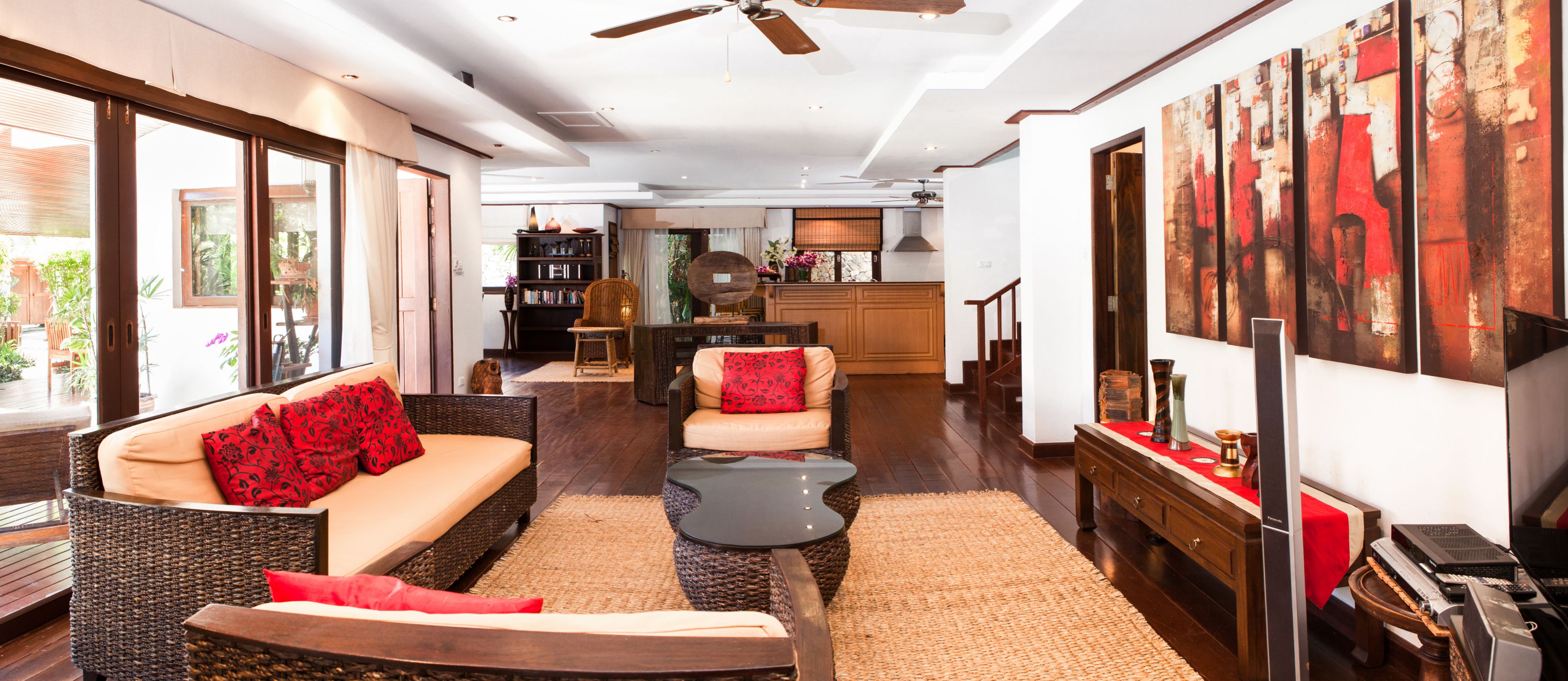 A spacious living area with a sofa, armchair, and coffee table, a kitchen in the background, and a large abstract painting on the wall.