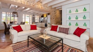 Ein geräumiges Wohnzimmer mit zwei weißen Sofas, roten Kissen, einem Glastisch und einer Steinwand.