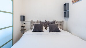Ein Schlafzimmer mit einem Bett, zwei Kissen, einem Kopfteil, einem Nachttisch, einer Lampe und einem Wandregal.