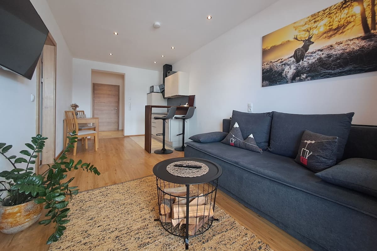 Una sala de estar moderna con un sofá gris, una mesita redonda y un cuadro de un ciervo.