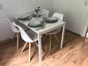 A dining table set with plates, glasses, and cutlery, surrounded by white chairs with wooden legs.