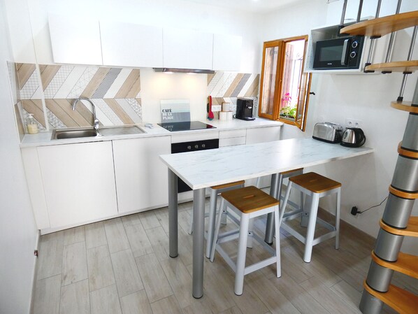 A modern kitchen with white cabinetry, a stainless steel sink, a built-in microwave, and a coffee machine. There are two stools and a white marble countertop. - Le Pouffre, renovated fisherman's house, air-conditioning, Wifi, small sea view (Sète)