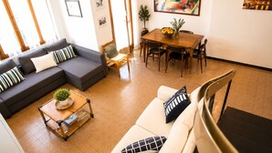 En stue med en sofa, et sofabord med en plante, et spisebord med stole og et billede på væggen.