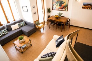 Uma sala de estar com um sofá, uma mesa de centro com uma planta, uma mesa de jantar com cadeiras e um quadro na parede.