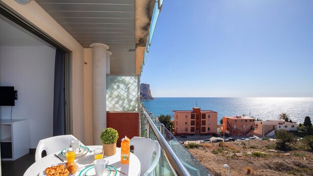 Ein Balkon mit Frühstückstisch, mit Blick auf die Küste, Gebäude und das Meer.